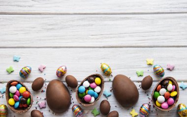 Beyaz ahşap arka planda renkli ve çikolatalı yumurtaları olan Paskalya kompozisyonu, yazı için boşluk. Üst manzara, düz uzanma. 