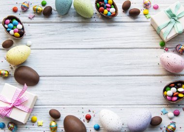 Beyaz ahşap arka planda renkli ve çikolatalı yumurtaları olan Paskalya kompozisyonu, yazı için boşluk. Üst manzara, düz uzanma. 
