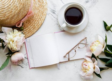 Flat lay blogger or freelancer workspace with a  notebook, pink peonies on a white marble table