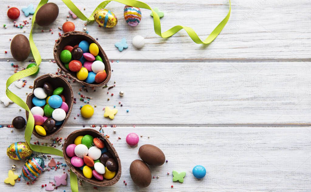 Easter composition with colorful and chocolate eggs on white wooden background, space for text. Top view, flat lay. 