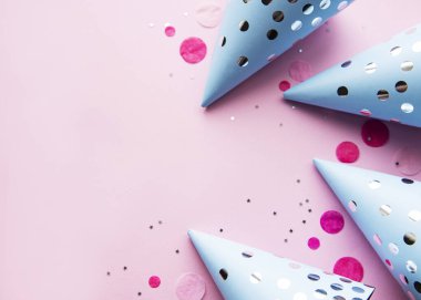 Mutlu yıllar ya da parti geçmişi. Doğum günü şapkaları ve pembe arka planda konfetileri olan düz yatış. Üst Manzara. Boşluğu kopyala.