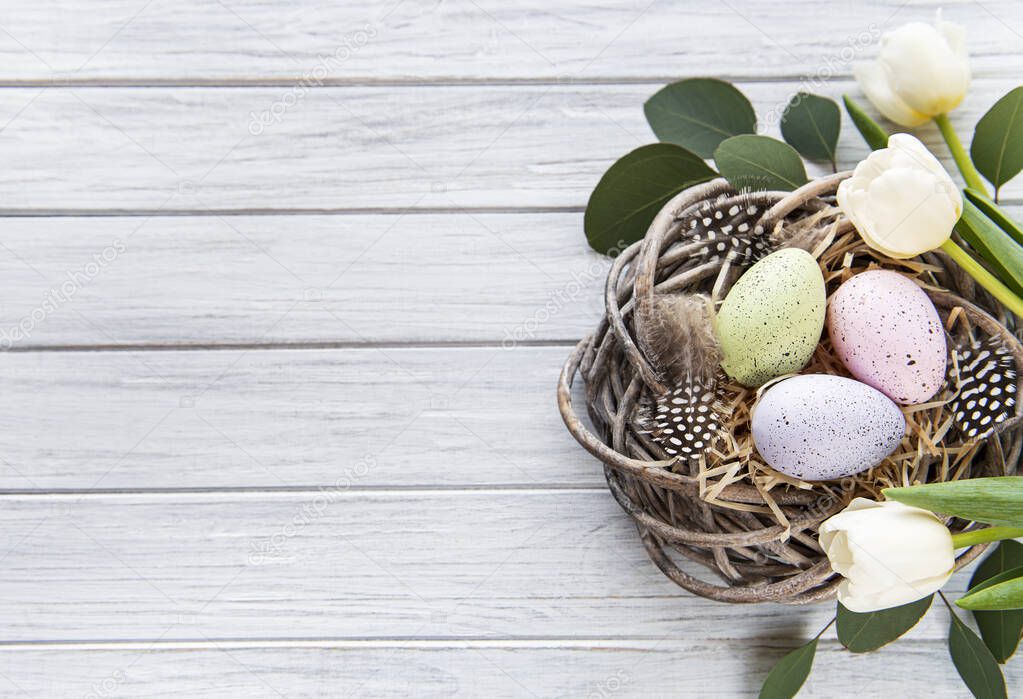 Easter background with colorful eggs in nest and pink tulips on a white wooden background. Top view with copy space