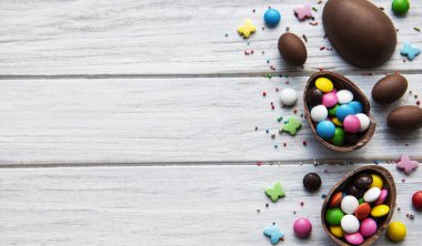 Beyaz ahşap arka planda renkli ve çikolatalı yumurtaları olan Paskalya kompozisyonu, yazı için boşluk. Üst manzara, düz uzanma. 