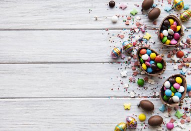 Beyaz ahşap arka planda renkli ve çikolatalı yumurtaları olan Paskalya kompozisyonu, yazı için boşluk. Üst manzara, düz uzanma. 