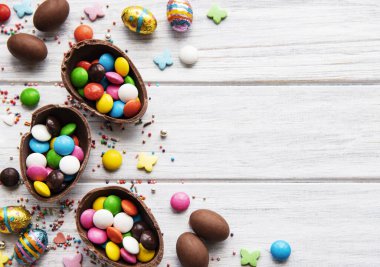 Beyaz ahşap arka planda renkli ve çikolatalı yumurtaları olan Paskalya kompozisyonu, yazı için boşluk. Üst manzara, düz uzanma. 