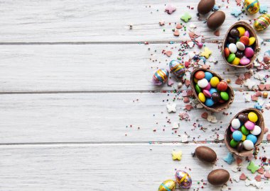 Beyaz ahşap arka planda renkli ve çikolatalı yumurtaları olan Paskalya kompozisyonu, yazı için boşluk. Üst manzara, düz uzanma. 