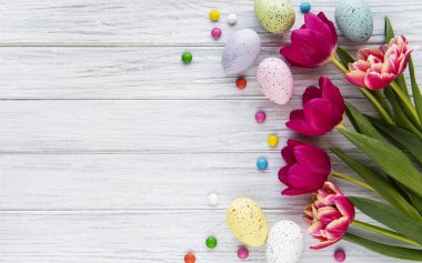 Beyaz ahşap arka planda renkli yumurtalar, laleler ve çikolata şekerli Paskalya kompozisyonu, yazı için yer. Üst manzara, düz uzanma. 