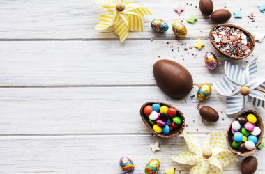 Beyaz ahşap arka planda renkli ve çikolatalı yumurtaları olan Paskalya kompozisyonu, yazı için boşluk. Üst manzara, düz uzanma. 