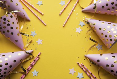 Happy birthday or party background.  Flat Lay wtih birthday hats, confetti and ribbons on yellow background. Top View.  Copy space.