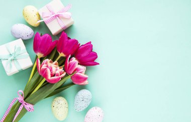 Bahar lale çiçekleri, Paskalya yumurtaları ve pastel yeşil arka planda hediye kutusu. Paskalya için selamlar. Üst manzara, düz uzanma.