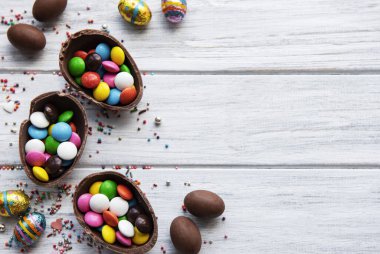 Beyaz ahşap arka planda renkli ve çikolatalı yumurtaları olan Paskalya kompozisyonu, yazı için boşluk. Üst manzara, düz uzanma. 
