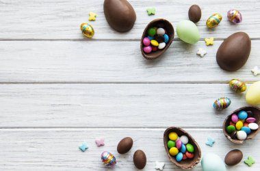 Beyaz ahşap arka planda renkli ve çikolatalı yumurtaları olan Paskalya kompozisyonu, yazı için boşluk. Üst manzara, düz uzanma. 
