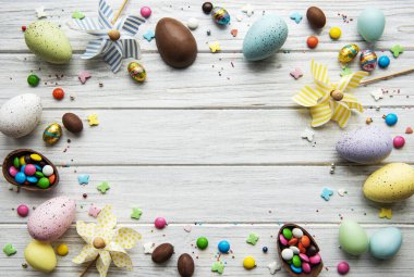Beyaz ahşap arka planda renkli ve çikolatalı yumurtaları olan Paskalya kompozisyonu, yazı için boşluk. Üst manzara, düz uzanma. 