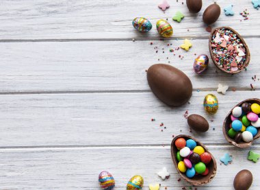 Beyaz ahşap arka planda renkli ve çikolatalı yumurtaları olan Paskalya kompozisyonu, yazı için boşluk. Üst manzara, düz uzanma. 