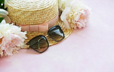 Tatil yaz geçmişi. Beyaz ahşap arka planda pembe peonies, güneş gözlüğü ve şapka.