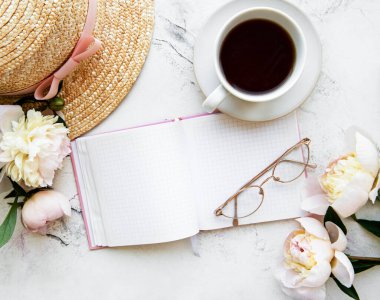 Flat lay blogger or freelancer workspace with a  notebook, pink peonies on a white marble table