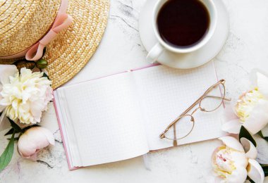 Flat lay blogger or freelancer workspace with a  notebook, pink peonies on a white marble table