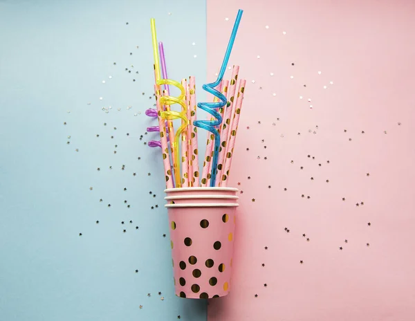 Birthday party caps,  paper straws and confetti  on pink and blue background
