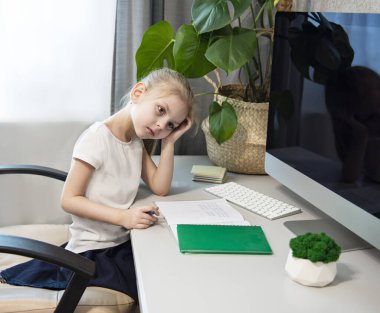 Koronavirüs salgınını karantina altına almak için evinizde kalın. Sarı saçlı küçük kız bir masaya oturur ve ödevlerini yapar.. 