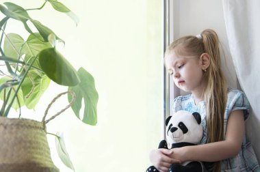 Evdeki pencerenin yanında üzgün bir kız çocuğu. Karantinaya alın. Koronavirüs salgını. Evde kal konsepti.