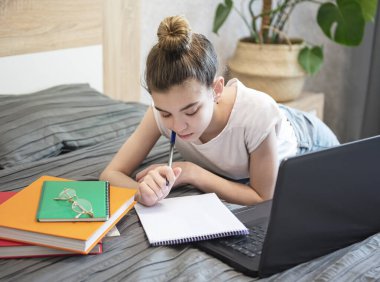 Genç kız evde dizüstü bilgisayar kullanıyor. Uzaklık öğrenme kavramı. 