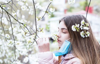 Genç bir kız maskesini çıkarıp bahar çiçeklerinin kokusunu içine çekiyor. Karantina kavramının sonu