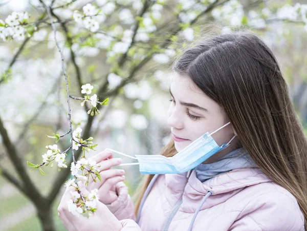 A young girl takes off the mask and breathe in the smell  spring flowers. End of quarantine concept