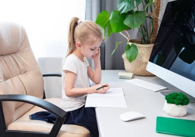 Koronavirüs salgınını karantina altına almak için evinizde kalın. Sarı saçlı küçük kız bir masaya oturur ve ödevlerini yapar.. 