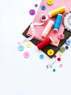 Beyaz arka planda aksesuar ve kumaş dikmek. Dikiş iplikleri, iğneler, iğneler, kumaşlar, düğmeler ve dikiş santimetresi. Üst manzara, düz uzanma.