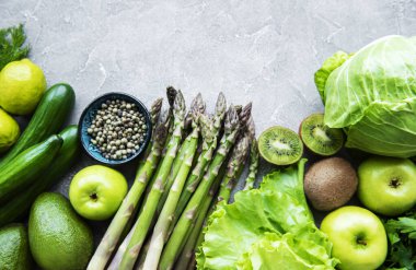 Sağlıklı vejetaryen gıda konsepti, detoks diyeti için taze yeşil gıda seçimi, elma, salatalık, kuşkonmaz, avokado, limon, beton arka planda salata üstü görünümü.