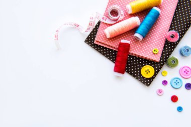 Beyaz arka planda aksesuar ve kumaş dikmek. Dikiş iplikleri, iğneler, iğneler, kumaşlar, düğmeler ve dikiş santimetresi. Üst manzara, düz uzanma.