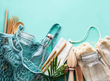 Sıfır atık, plastiksiz ve çevre dostu yaşam tarzı. Pamuklu örgü çanta, cam şişe, kavanoz ve yeşil arka planda bambu çatal bıçak takımı. Düz yatıyordu. 