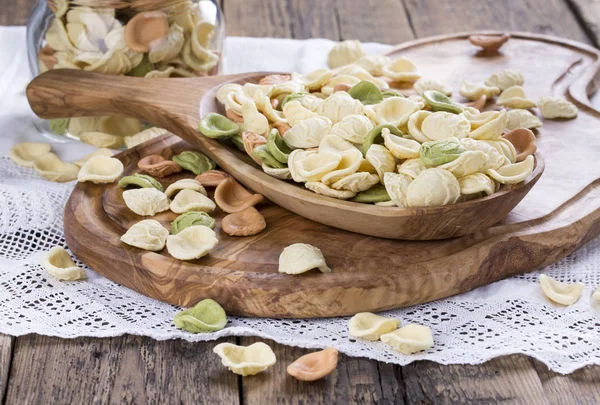 Ongekookt kleurrijke orecchiette in een houten kom. Italiaanse pasta. — Stockfoto