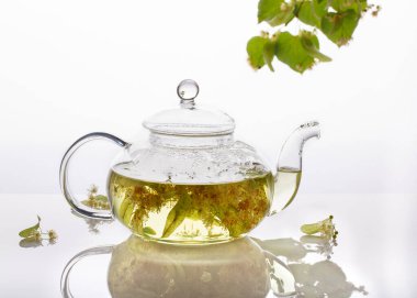 Şeffaf bir çaydanlıkta ıhlamur çayı. Beyaz arka planda bitkisel limon ağacı çayı olan cam çaydanlık. Şifalı bitki, bitkisel çaylar ve tentürler için kullanılan çiçekler..