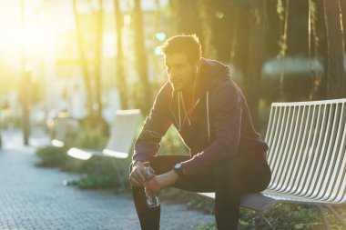 Şişe su ile bankta oturan atlet
