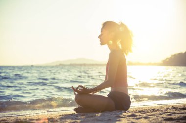 Genç kadın plajda yoga yapıyor..