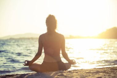 Genç kadın plajda yoga yapıyor..