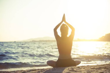 Genç kadın plajda yoga yapıyor..