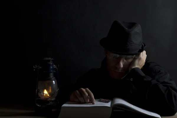 Людина в капелюсі читає книгу в темряві — стокове фото