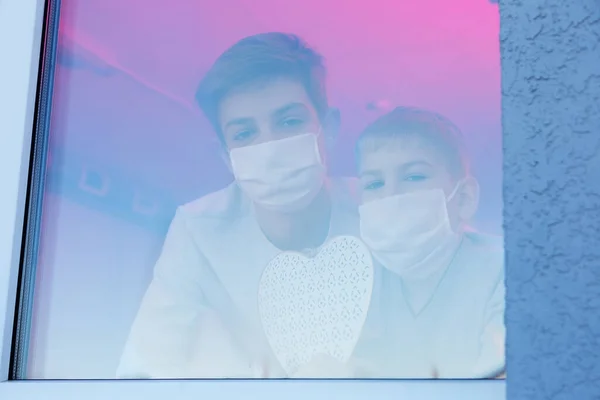 Дети в защитных масках, заглядывающие в окно больницы — стоковое фото