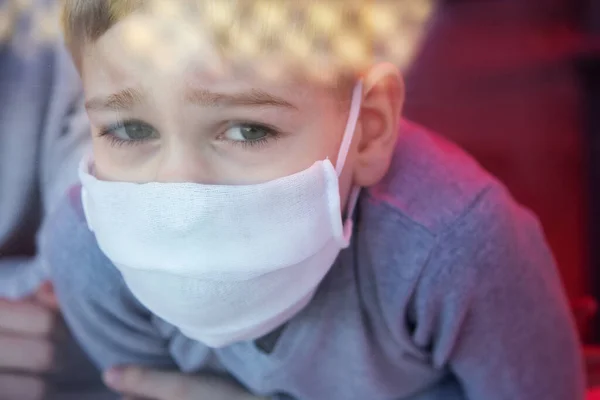 Koruyucu maskeler takan üzgün çocuk pencereden içeri giriyor. — Stok fotoğraf