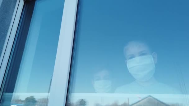 Niños con máscaras protectoras asomándose por la ventana de cerca — Vídeo de stock