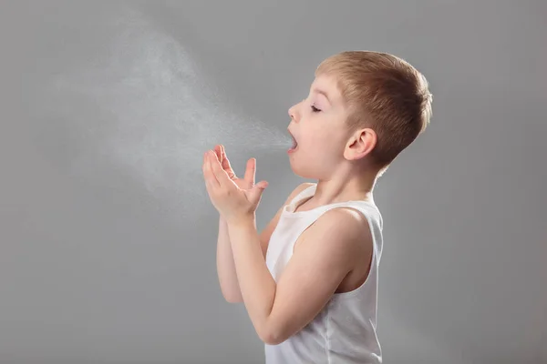 Niño malsano en ropa blanca estornudando muy duro sobre fondo gris Fotos De Stock