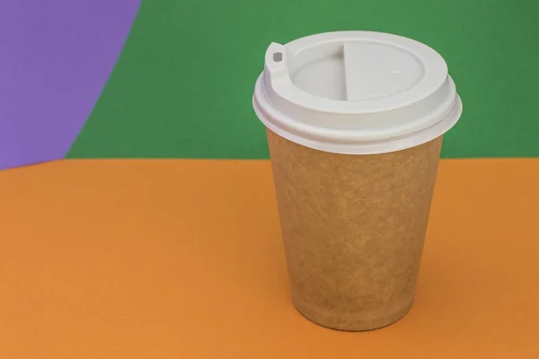Paper cup with coffee on bright orange and green background