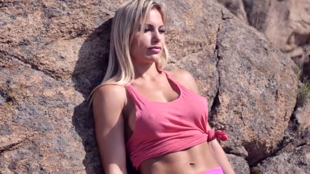 Una joven mujer se para cerca de una roca en un soleado mediodía caliente — Vídeos de Stock