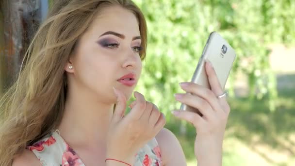 Uma jovem ajusta sua maquiagem com um telefone — Vídeo de Stock