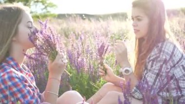 Kızlar Eflatun çiçekler ile sahada oturan