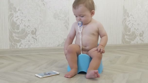 Bebé sentado en una olla mira en el teléfono — Vídeos de Stock