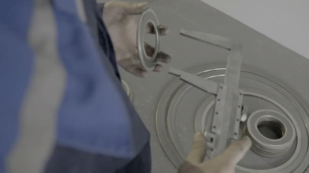 Un trabajador cualificado en azul mide las dimensiones de una pieza utilizando una pinza vernier en la fábrica . — Vídeos de Stock