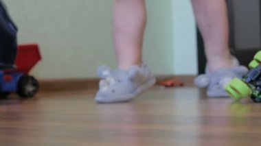 Terlikli çocuk elinde oyuncaklarla odada dolaşıyor.